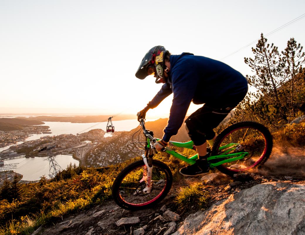 Person offroad bycycling on a mountain side, with city and sea behind